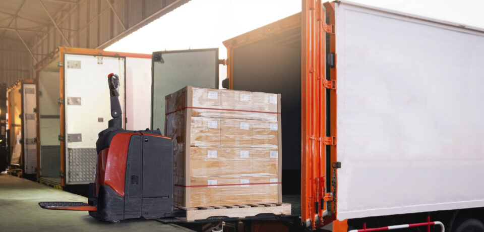 electric-forklift-loading-package-boxes-into-container-trucks-parked-loading-dock-warehouse